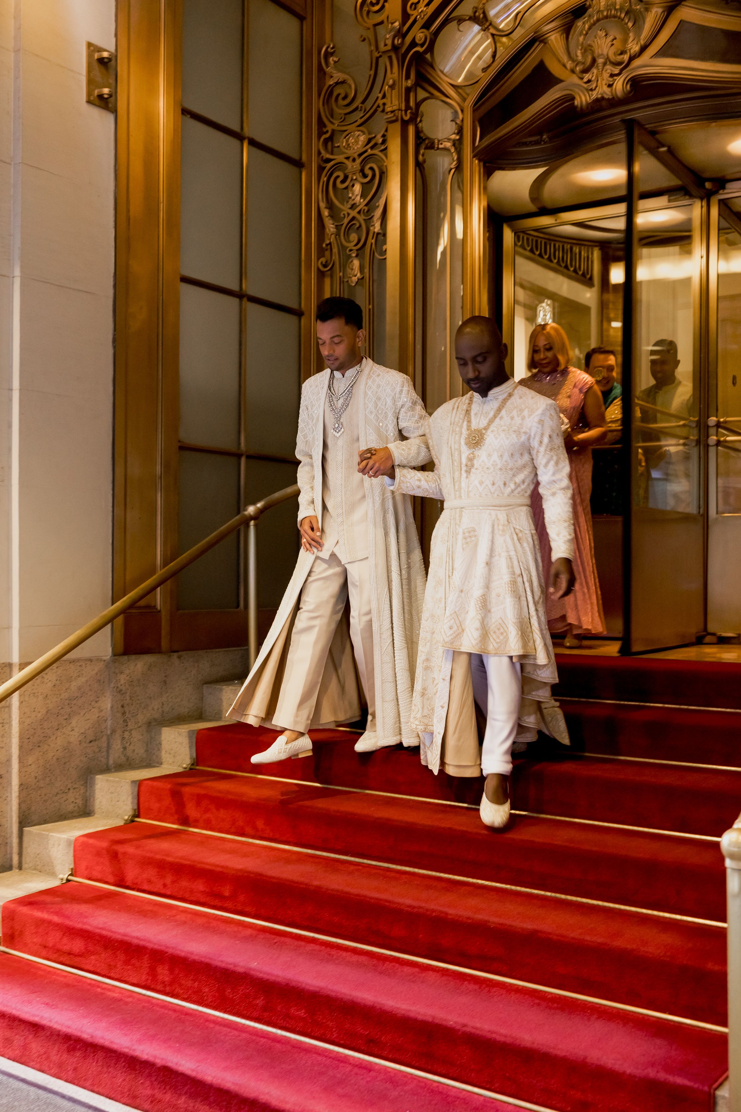 Wedding party descending elegant red carpeted stairs in formal white attire.