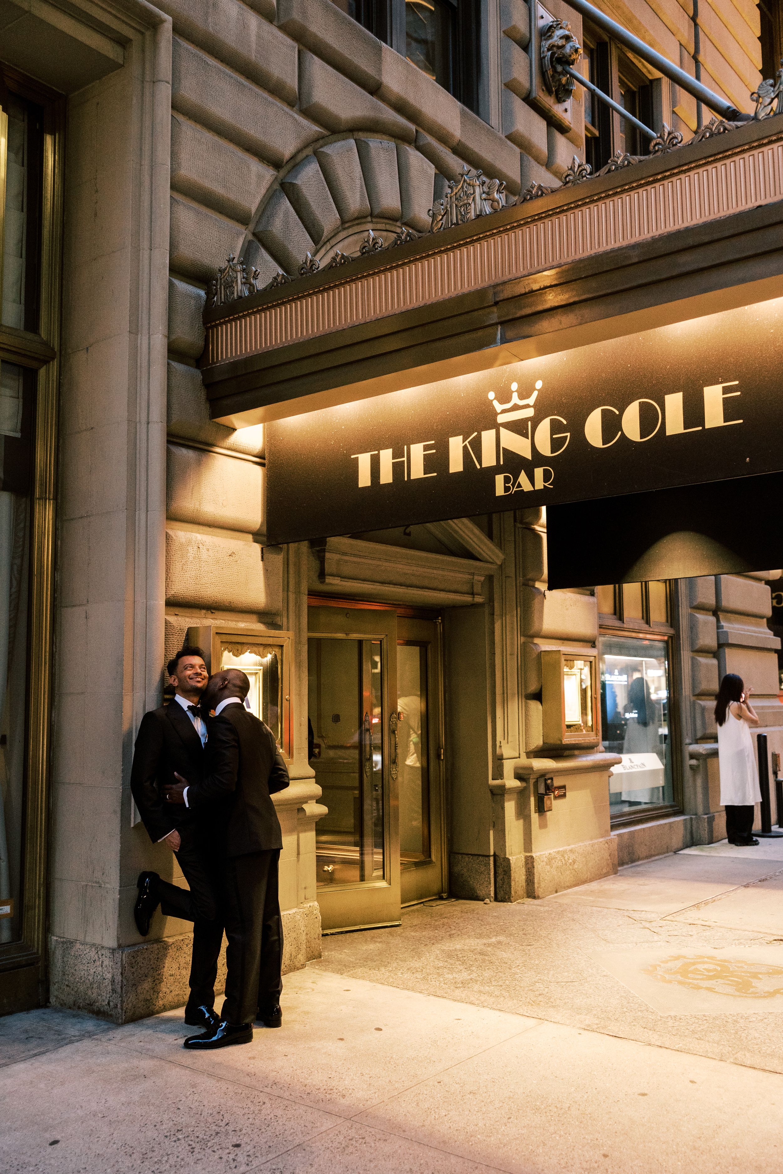 Nighttime view of the illuminated King Cole Bar entrance with formal event guests arriving.