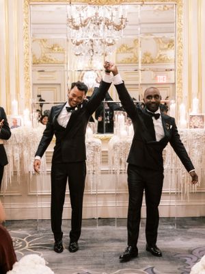 Groomsmen in black tuxedos perform synchronized dance moves at an elegant wedding reception.