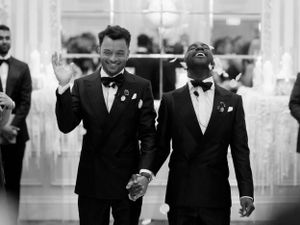 Wedding party members walking through an elegant white ballroom with crystal chandeliers.