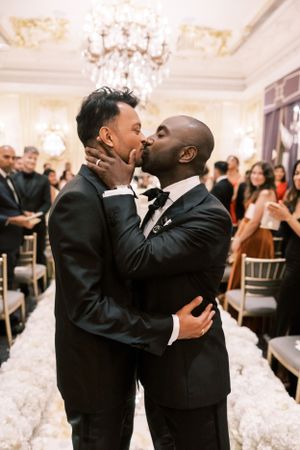 Two grooms share a romantic dance together in a white ballroom at their wedding celebration.