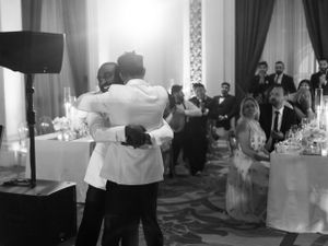 A black and white photo of a couple's first dance at a wedding reception while guests look on.