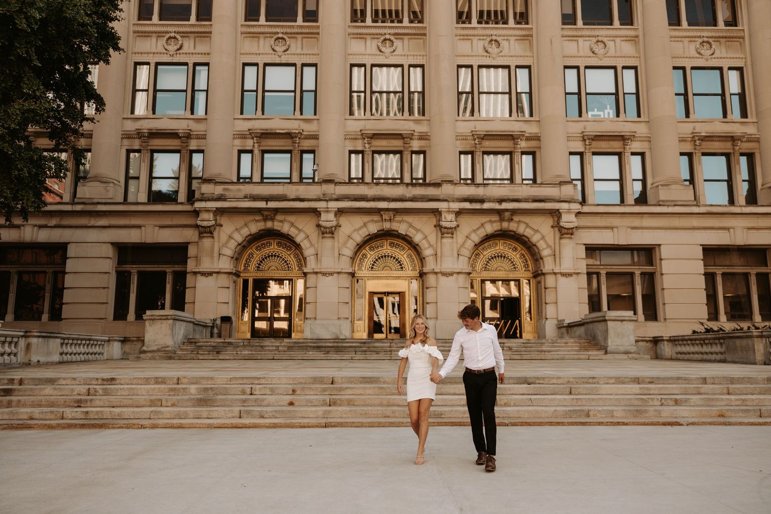 A couple walks together outside the downtown Omaha courthouse building with arched windows and ornate architectural details at sunset.