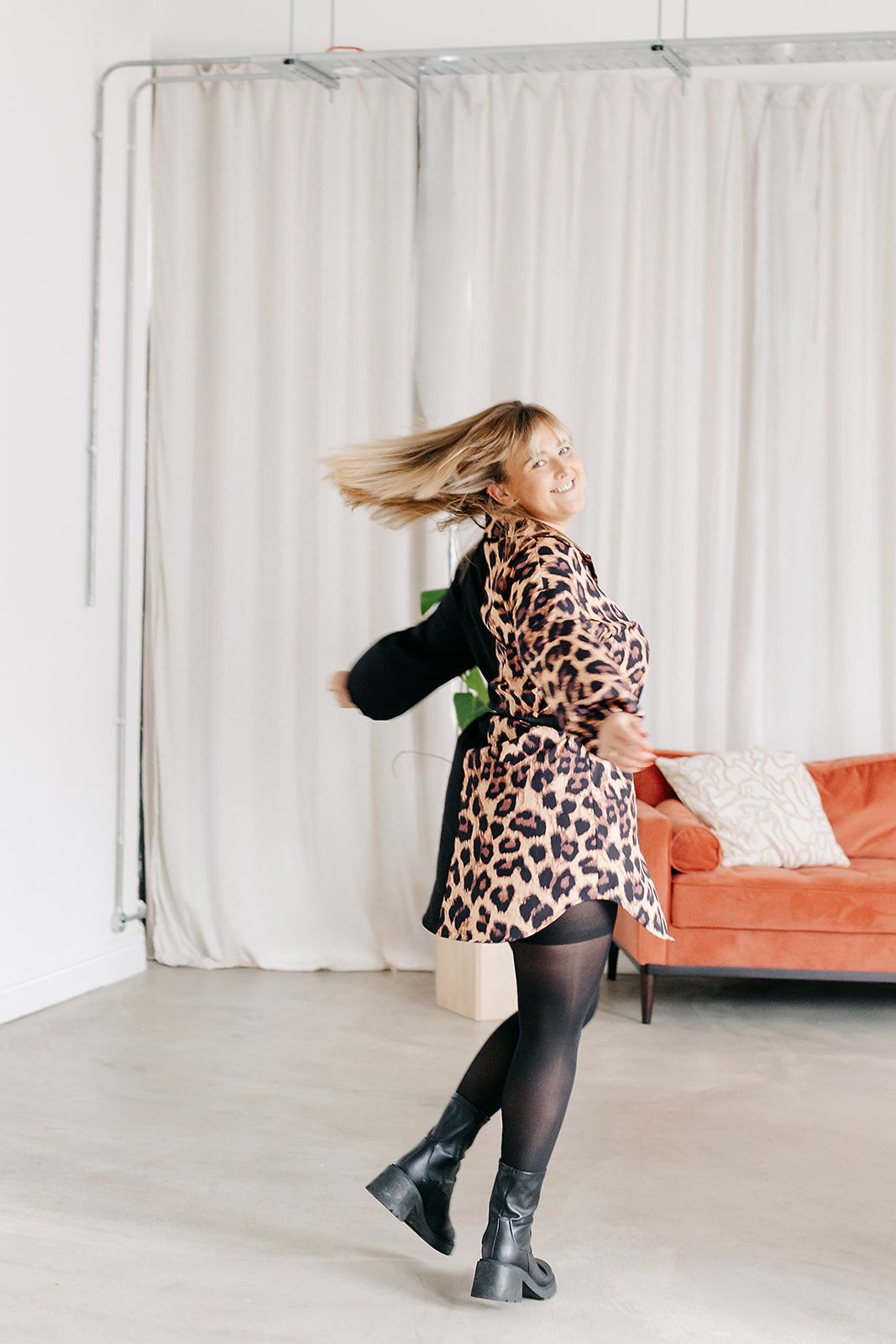 Person in leopard print sweater spins and dances in sequence across minimalist room with orange couch and white curtains.
