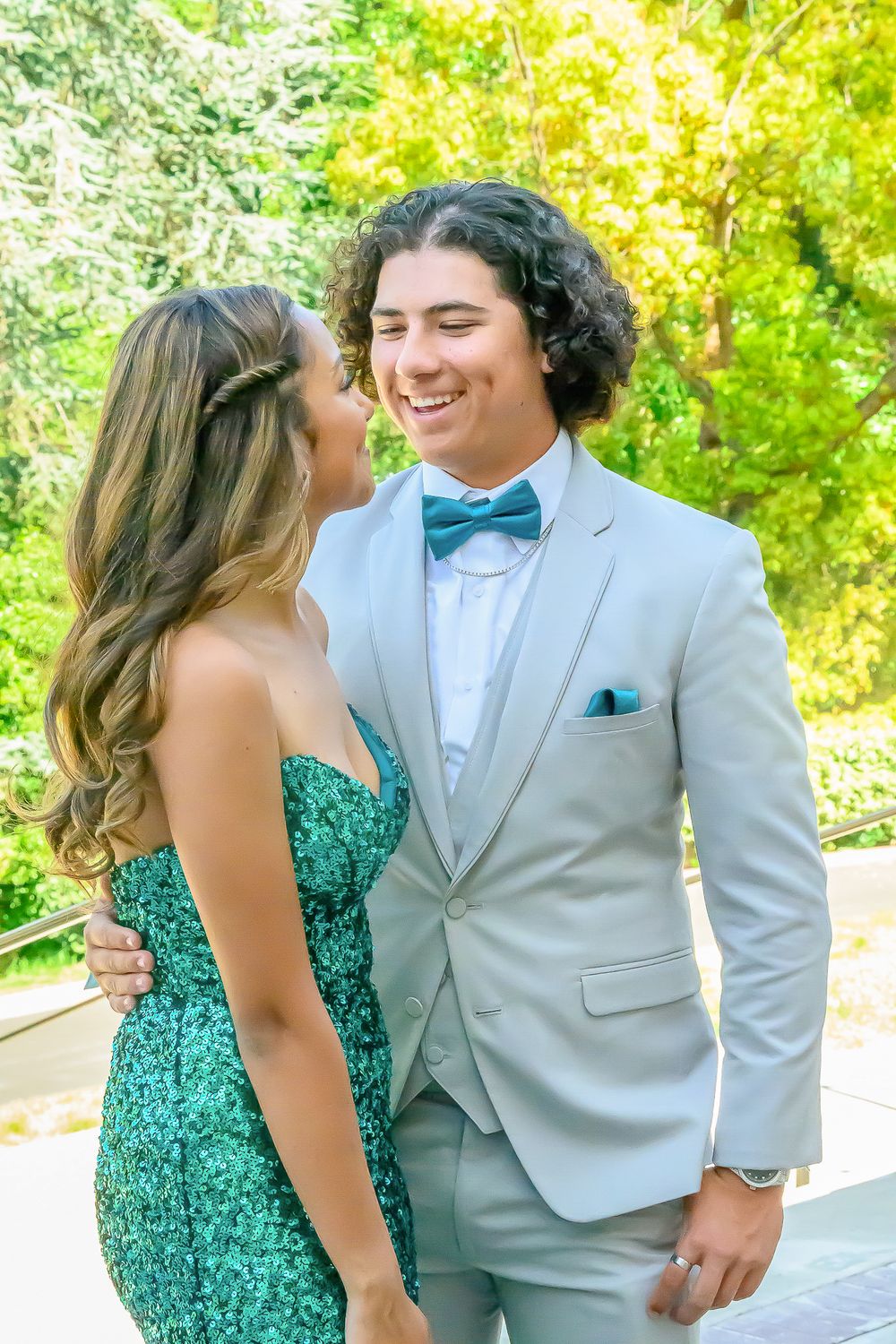 Formal couple in green dress and light gray suit posing together in a garden setting.