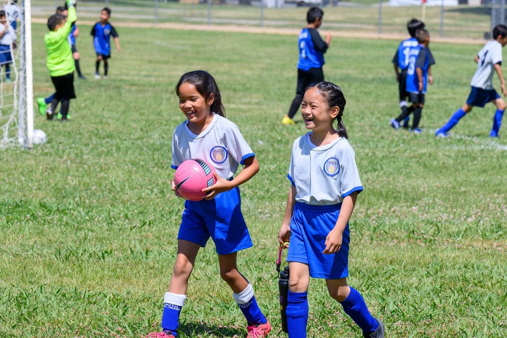 Youth soccer players in blue uniforms practicing drills on a grass field.