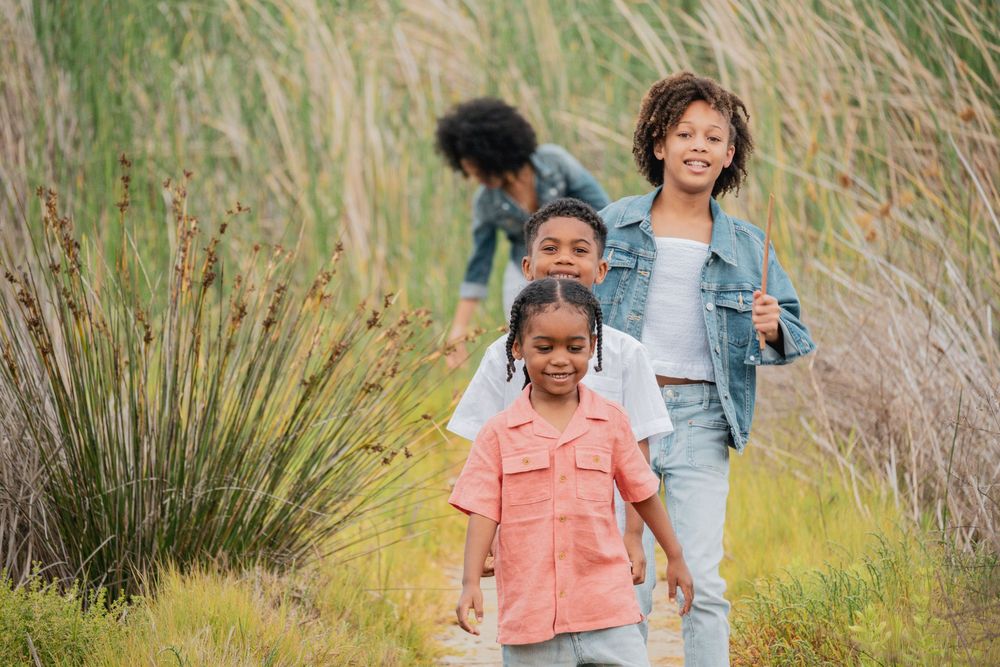 Family walking through tall golden grass during an outdoor photo session.