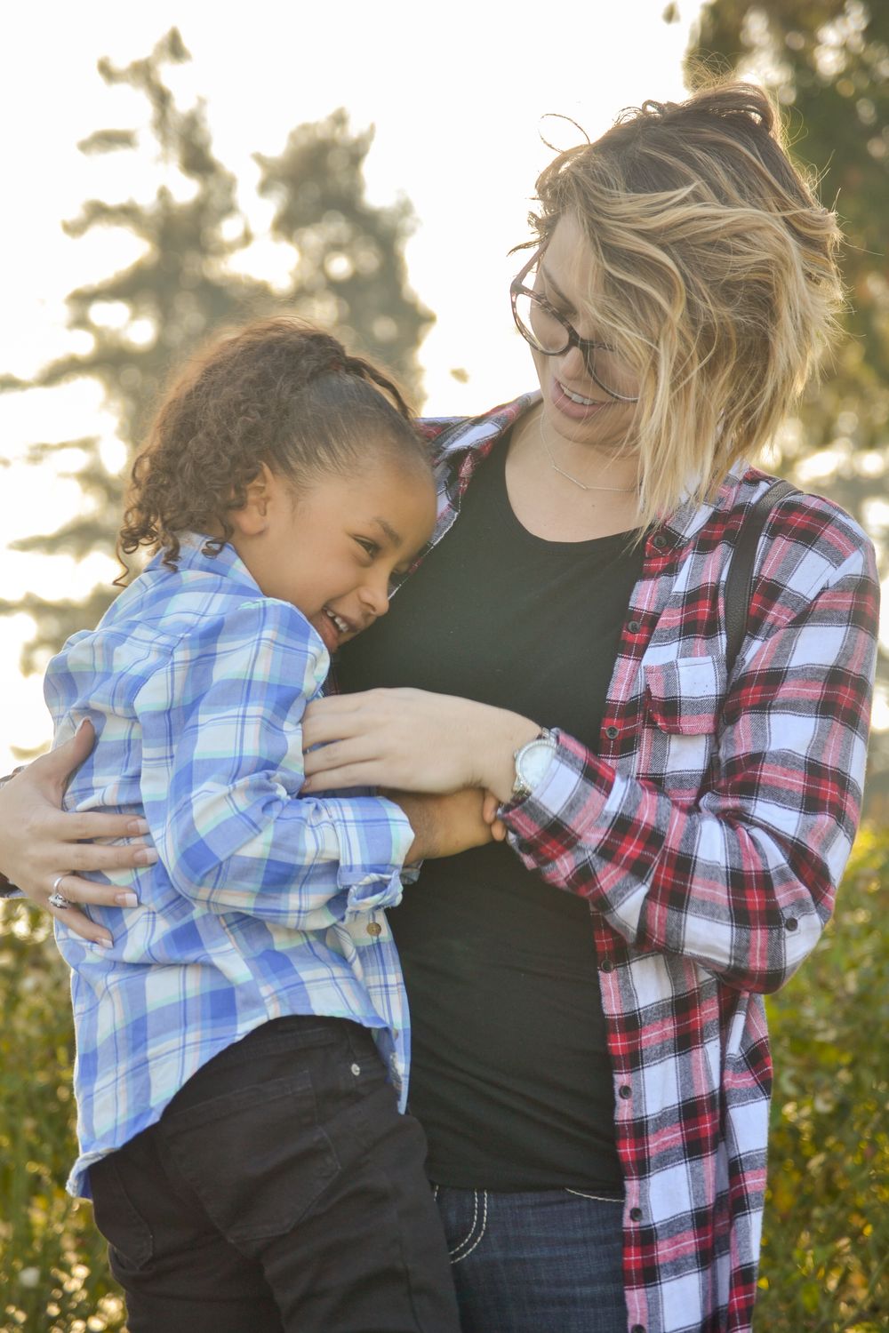 Family maternity photo with child hugging and laughing in golden sunlight.