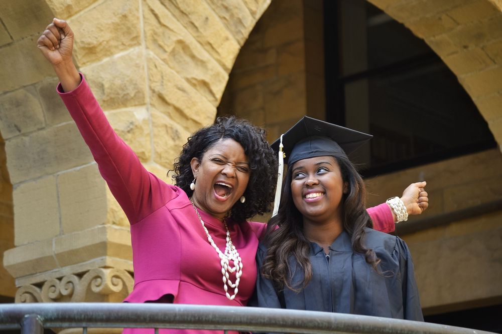 Graduates in caps and gowns celebrating with raised arms at commencement ceremony.