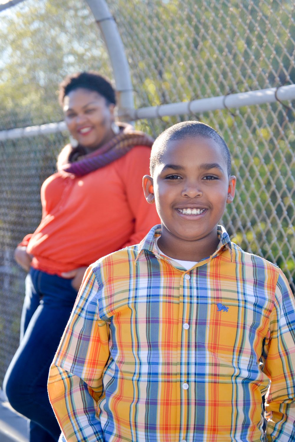 Cheerful expressions during an outdoor photoshoot against a chain link fence background.