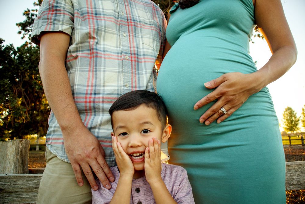 Maternity photo session outdoors with child playing peek-a-boo.