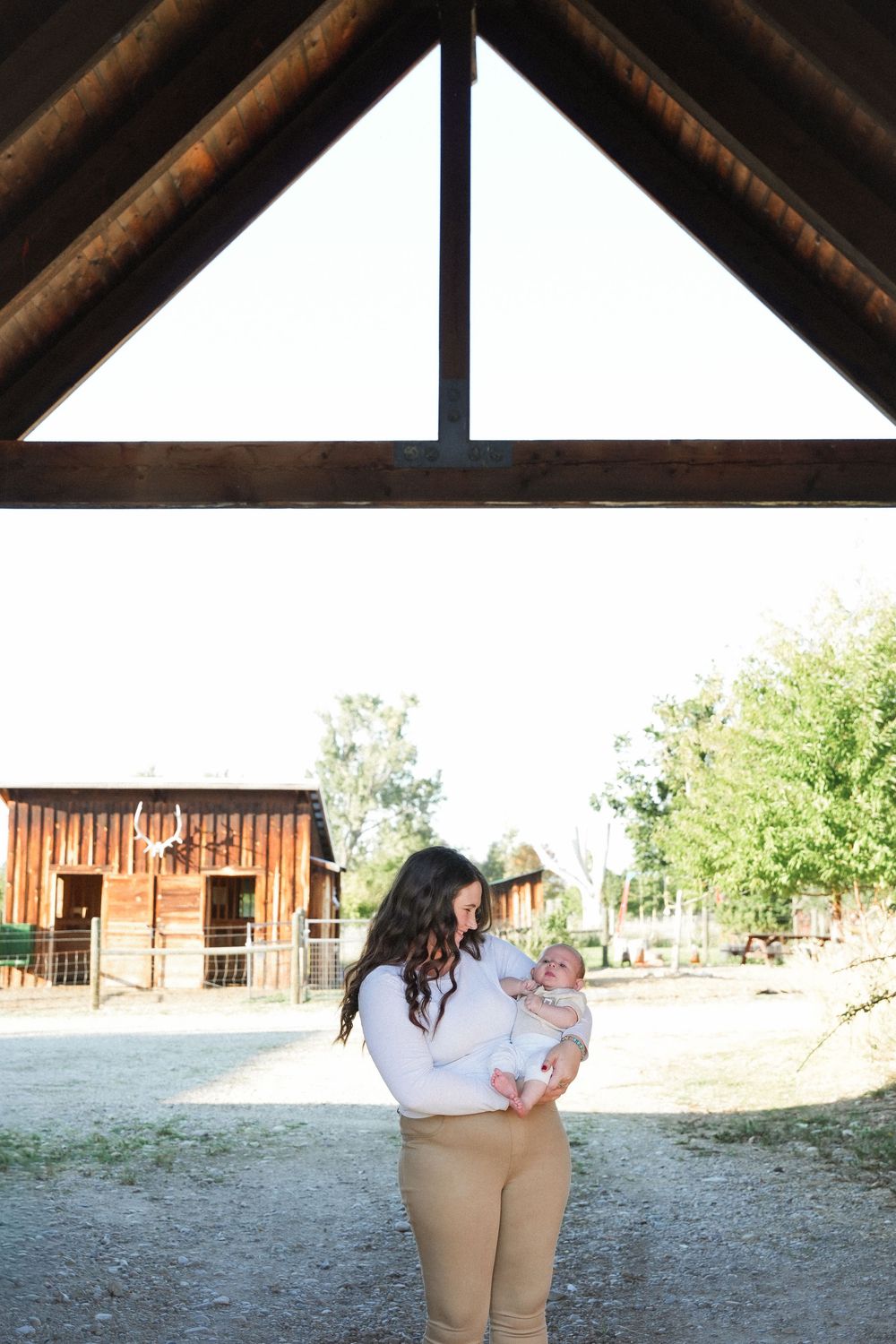 A person in khaki pants holds a small child while walking through a rustic outdoor setting with wooden buildings.