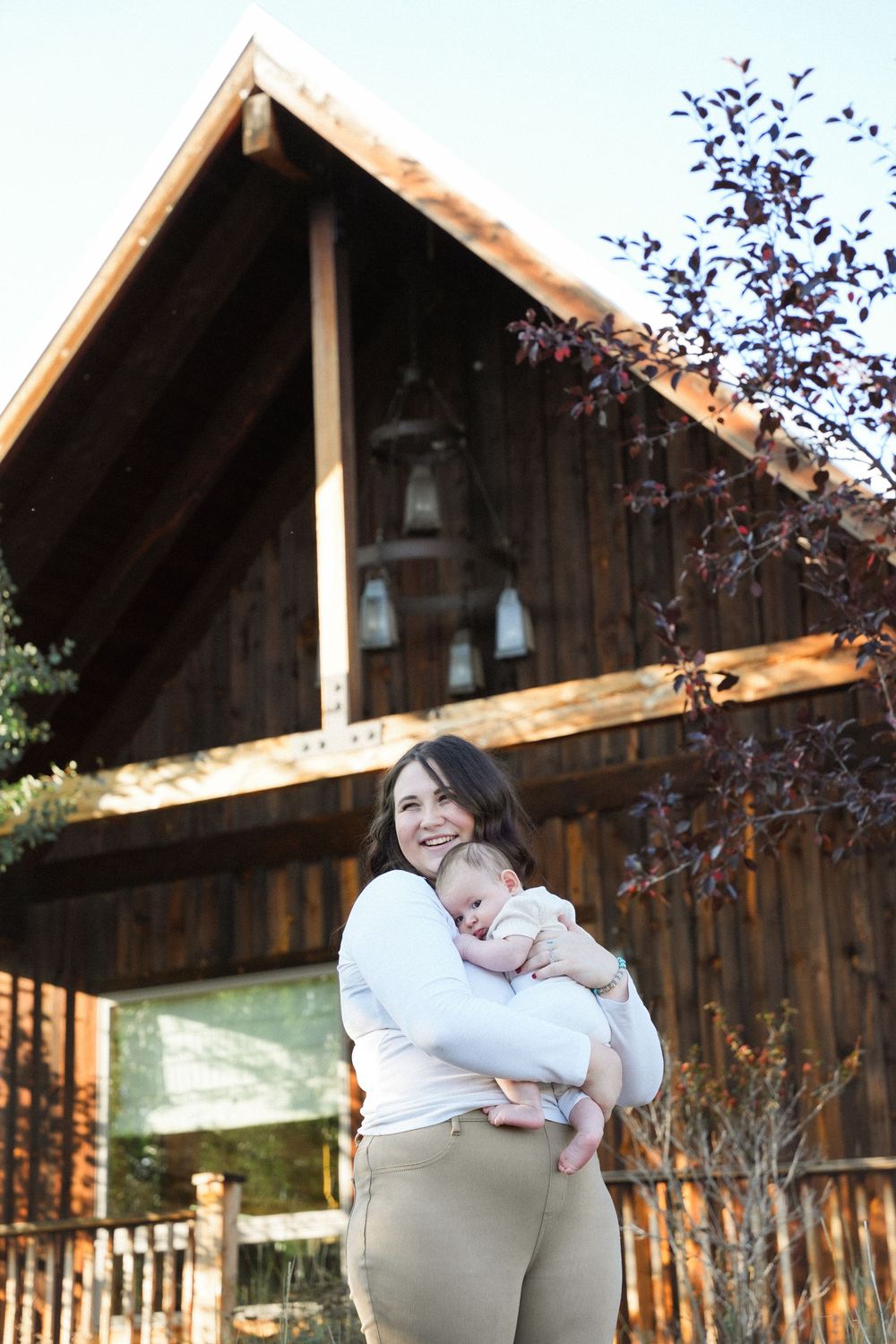A rustic wooden barn with hanging lanterns serves as the backdrop for a tender moment on a sunny day.
