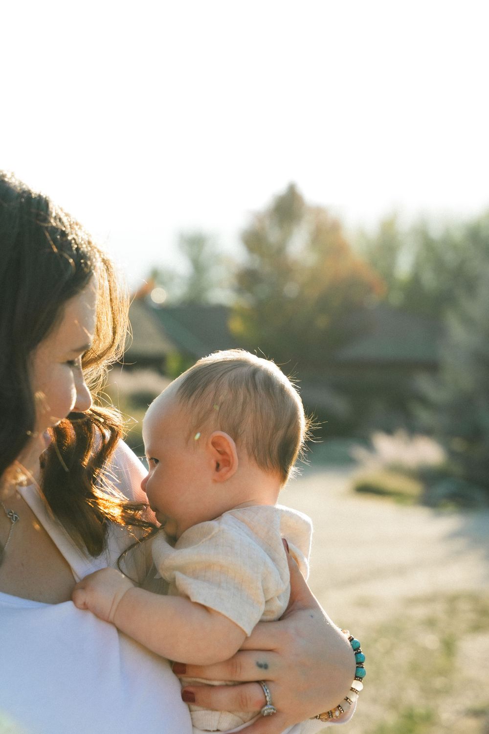 A tender moment captured in golden sunlight shows a parent holding a baby against their chest outdoors.