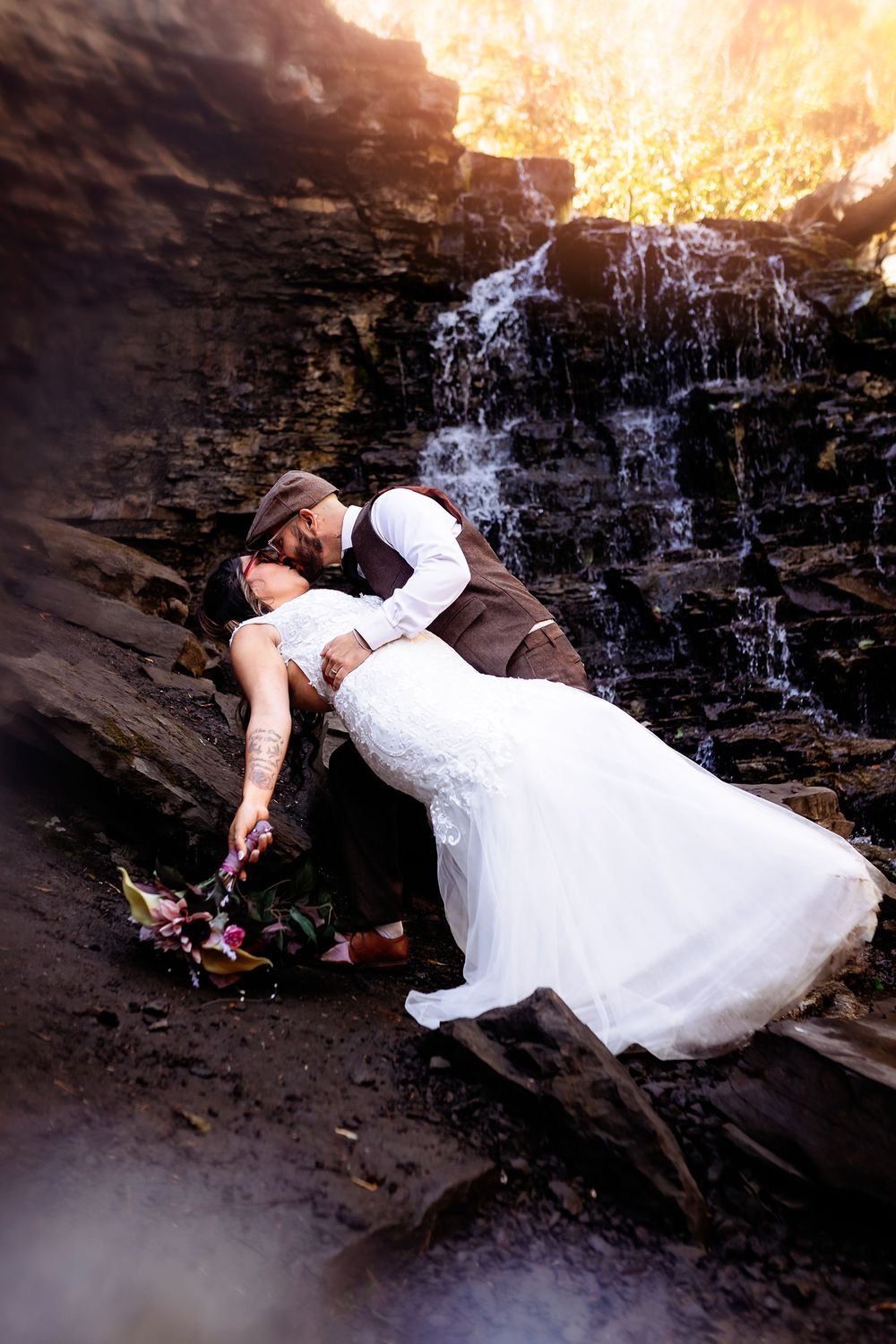 A dramatic wedding photo with a couple in a dip pose against a cascading waterfall backdrop.