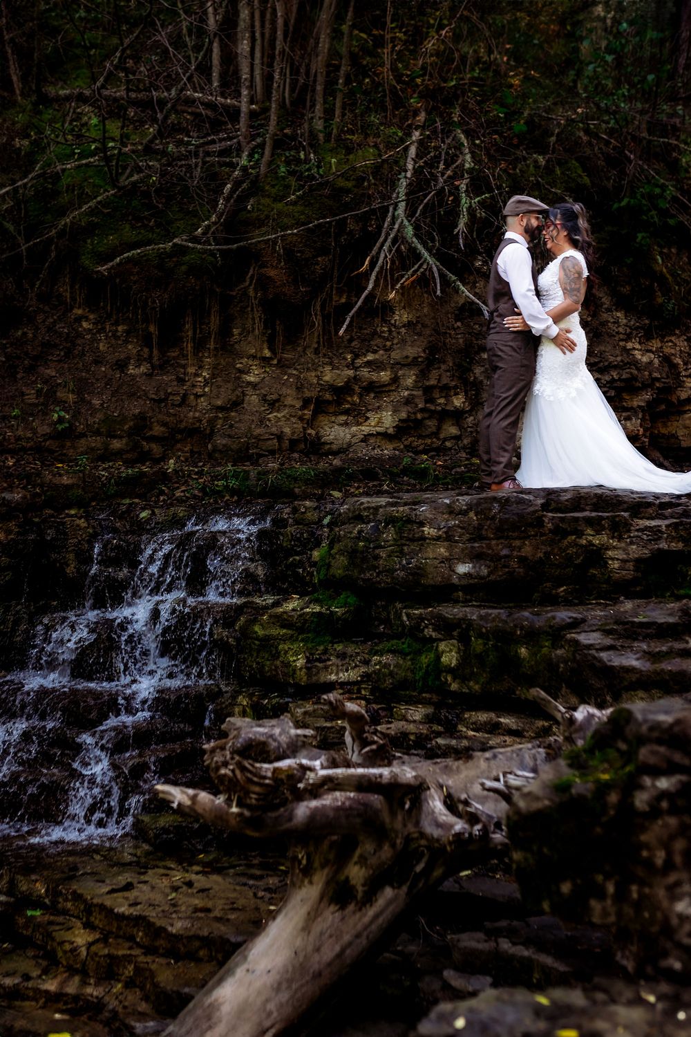 A romantic wedding photo shoot near a small cascading waterfall surrounded by mossy rocks.