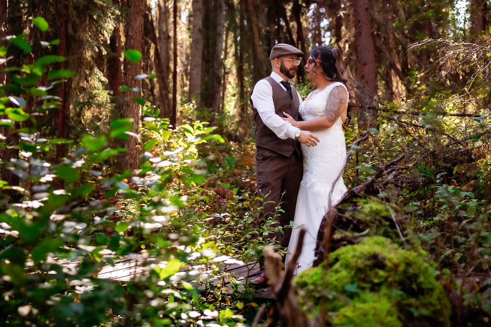 A wedding couple shares an intimate moment in a sunlit forest setting.