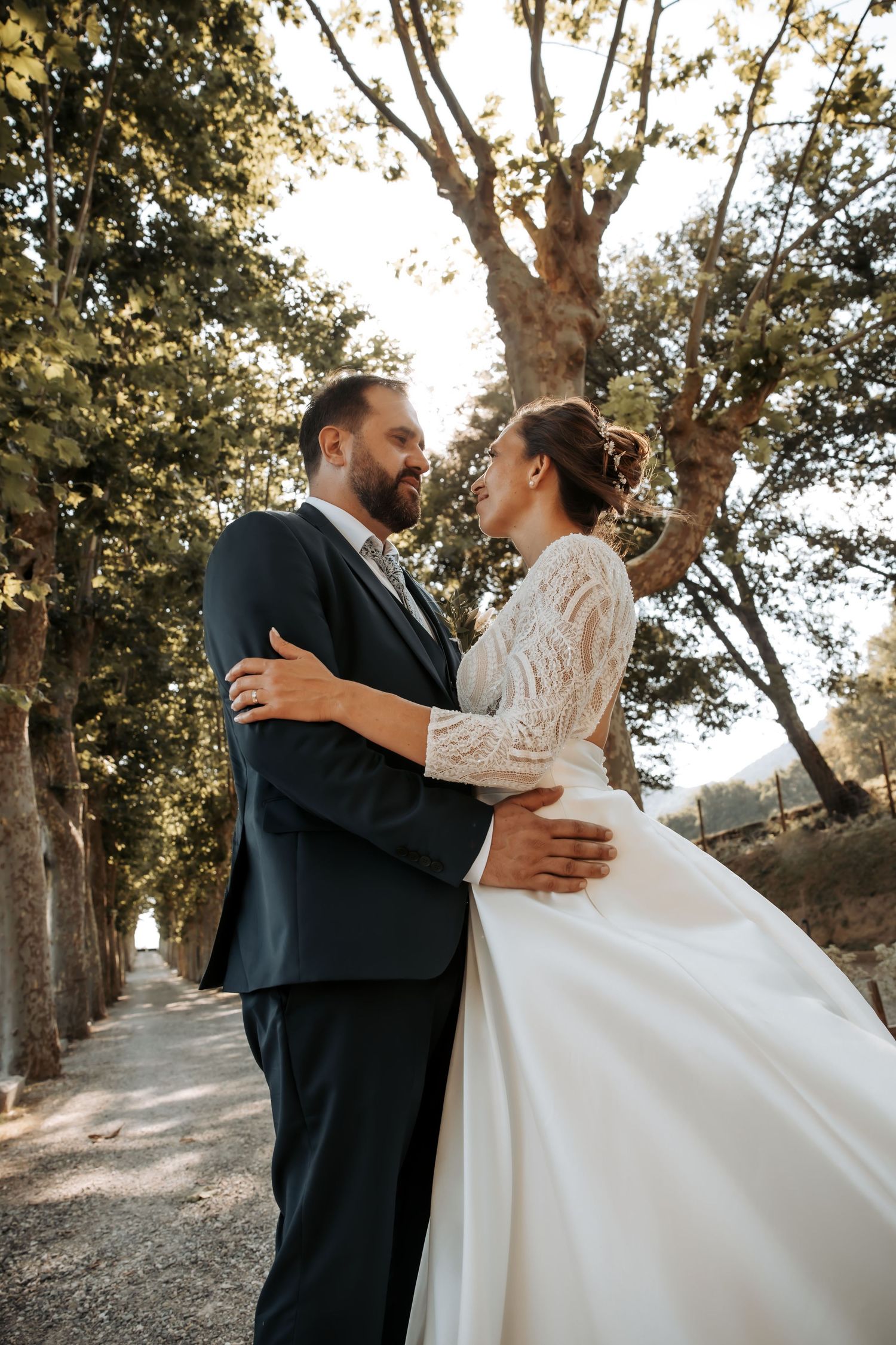 Joyful wedding couple dances under tree-lined path in golden sunlight. Domaine la Plume photographe mariage