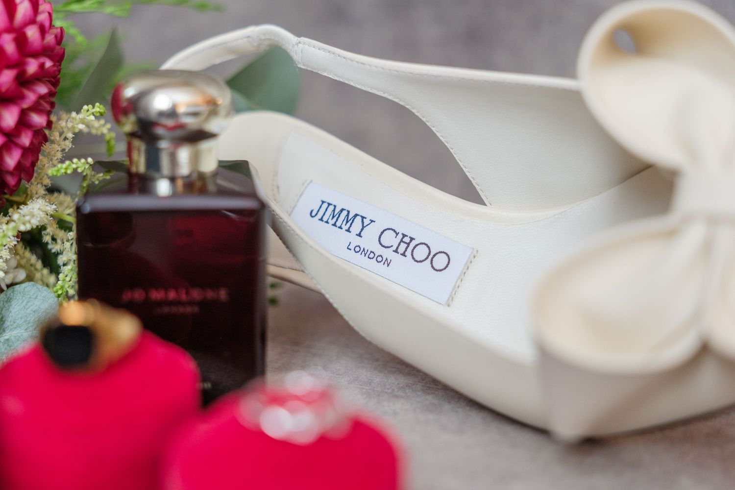 Jimmy Choo shoe label detail shown next to a dark perfume bottle and red decorative items.