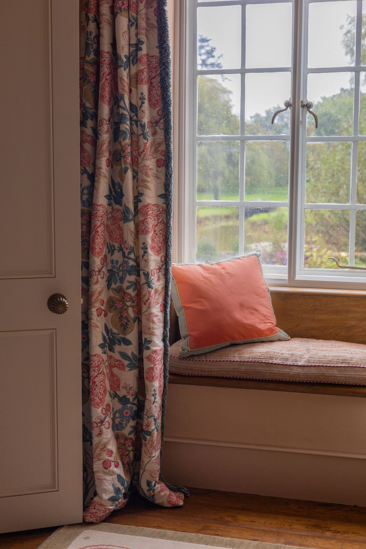 Cozy window seat with floral curtains and coral cushions in natural light.