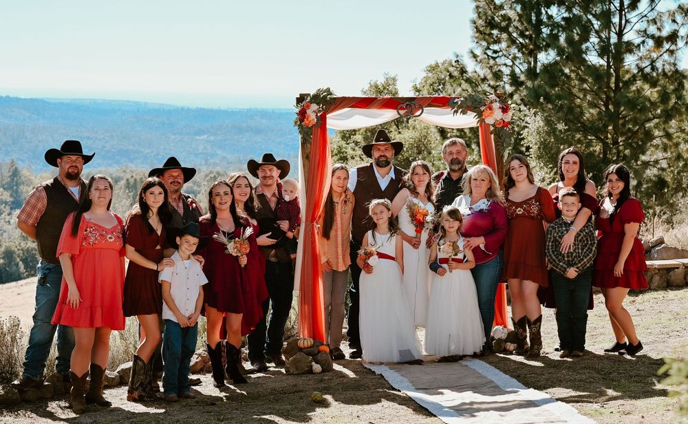Wedding party in red and white attire poses together on sunny mountain overlook during outdoor ceremony.