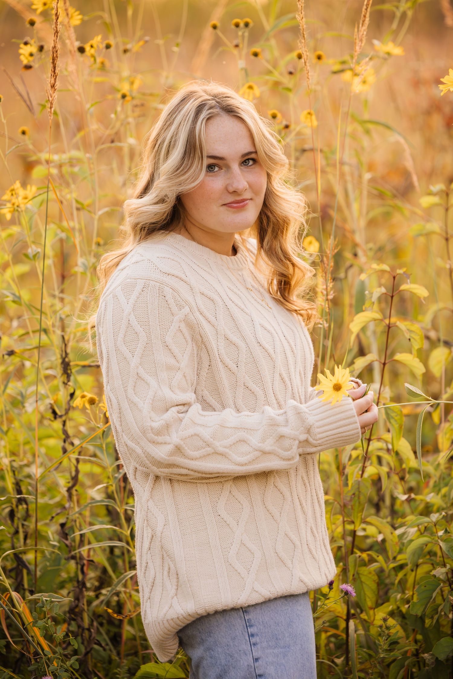 A cozy autumn portrait with a cream cable knit sweater against golden wildflowers at sunset.