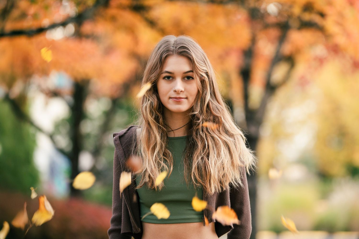 Long wavy hair blowing in autumn breeze as leaves fall from orange and yellow trees in background.
