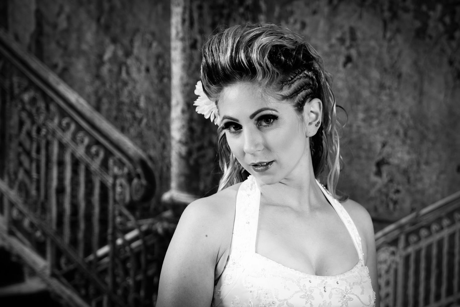 A black and white portrait featuring dramatic lighting and styling with a textured background and staircase.