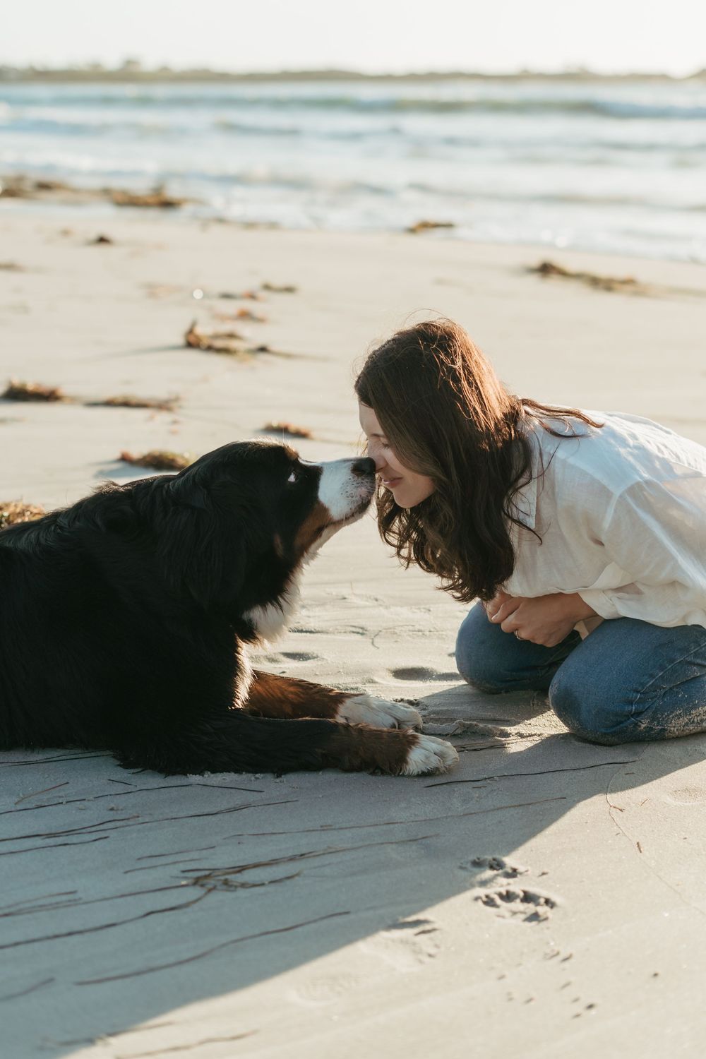 Young woman sharing a tender nose-to-nose moment with her Bernese Mountain Dog on a serene beach.