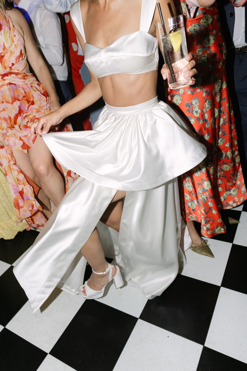 Dancing figure in white crop top and flowing pants moves energetically on a black and white checkered floor.