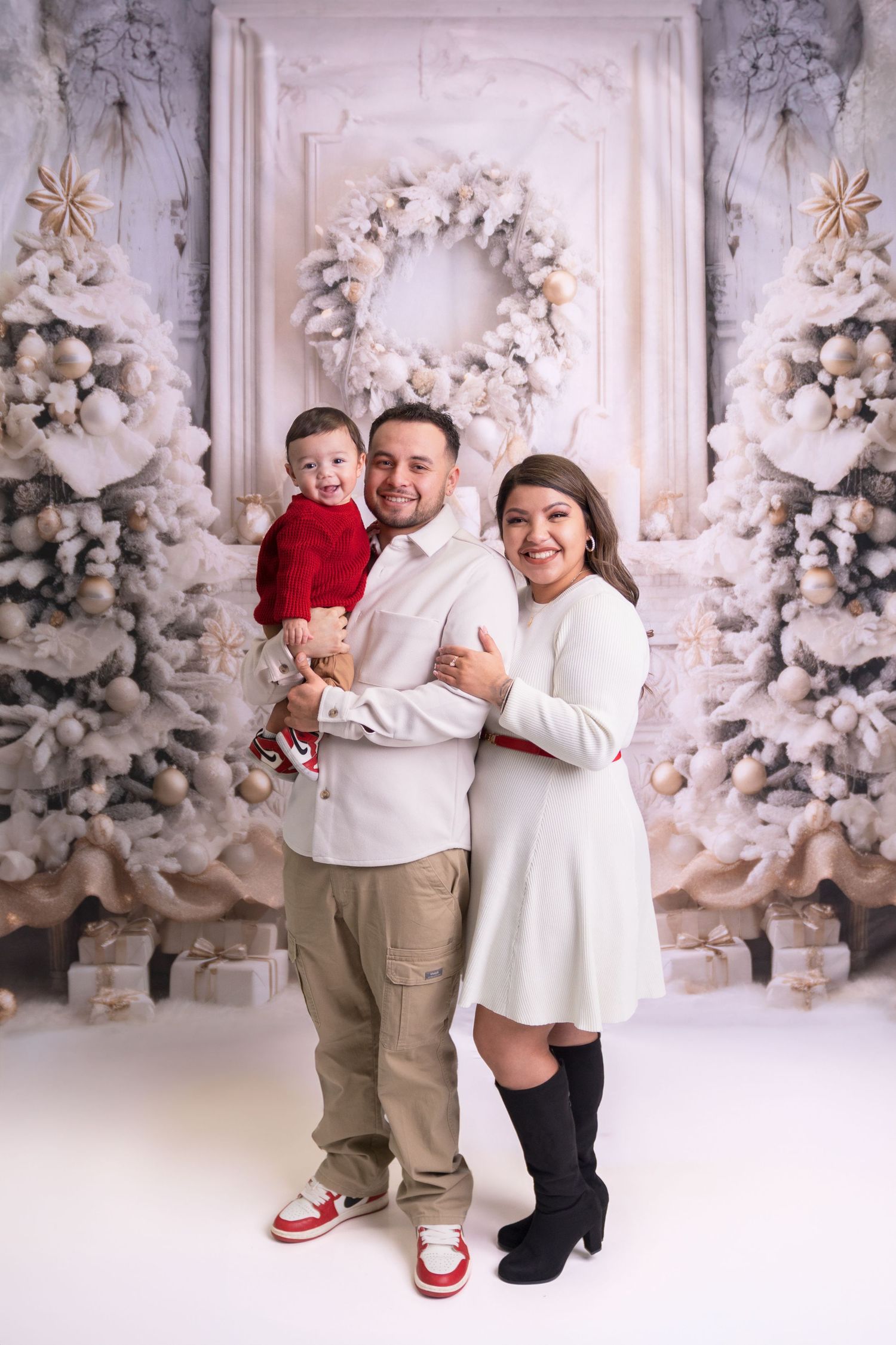 Joyful family photo against winter white Christmas backdrop with flocked trees.