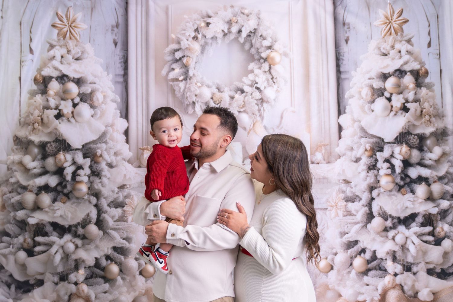 Family poses together in front of white Christmas trees and wreaths in a winter wonderland setting.