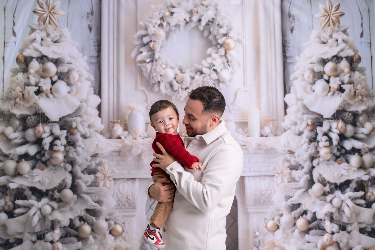 Holiday portrait session with family members wearing white and red against snowy Christmas backdrop.