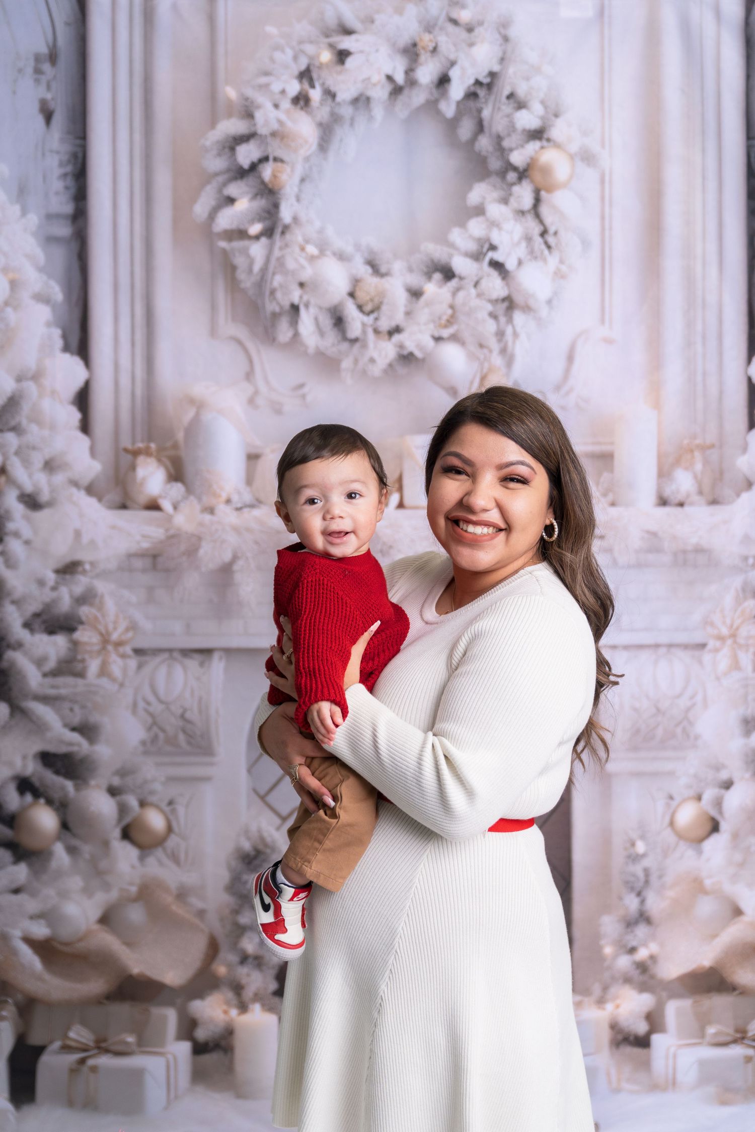 Family dressed in white poses together with decorative Christmas wreaths and trees in background.