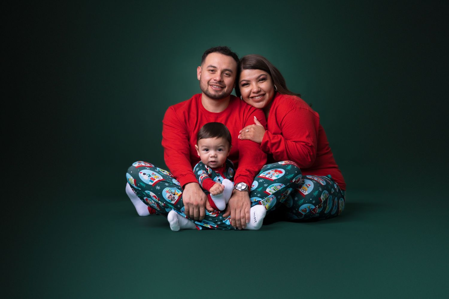 A family wearing matching red and patterned pajamas poses together against a dark green backdrop.