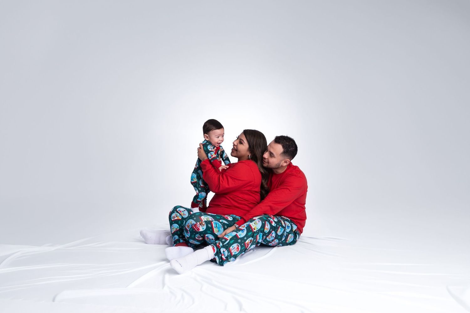 A family group lounges together on a white floor wearing coordinated holiday sleepwear.