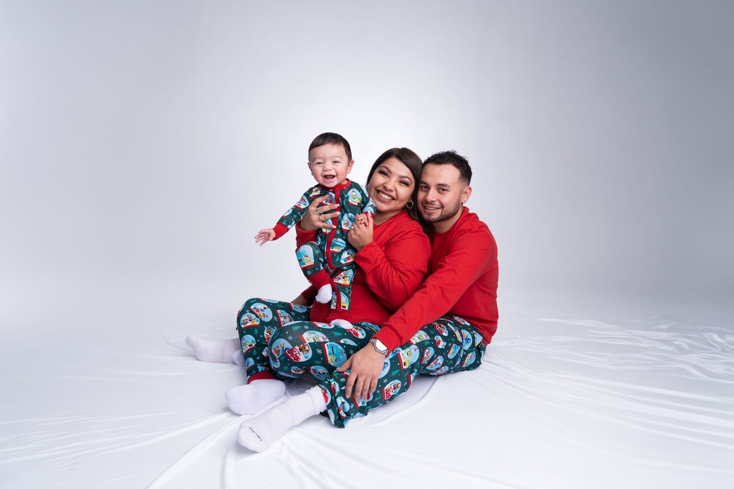 Three people in matching Christmas pajamas pose together on a white studio backdrop.