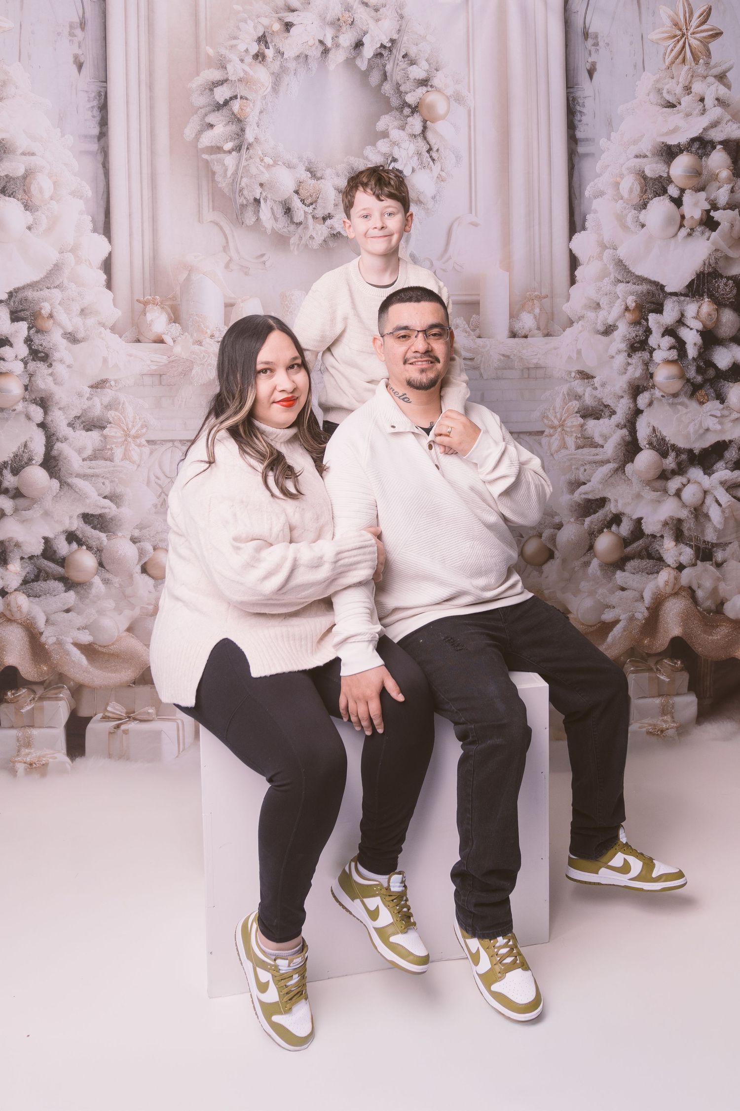 Family wearing matching white sweaters pose against winter wonderland backdrop.