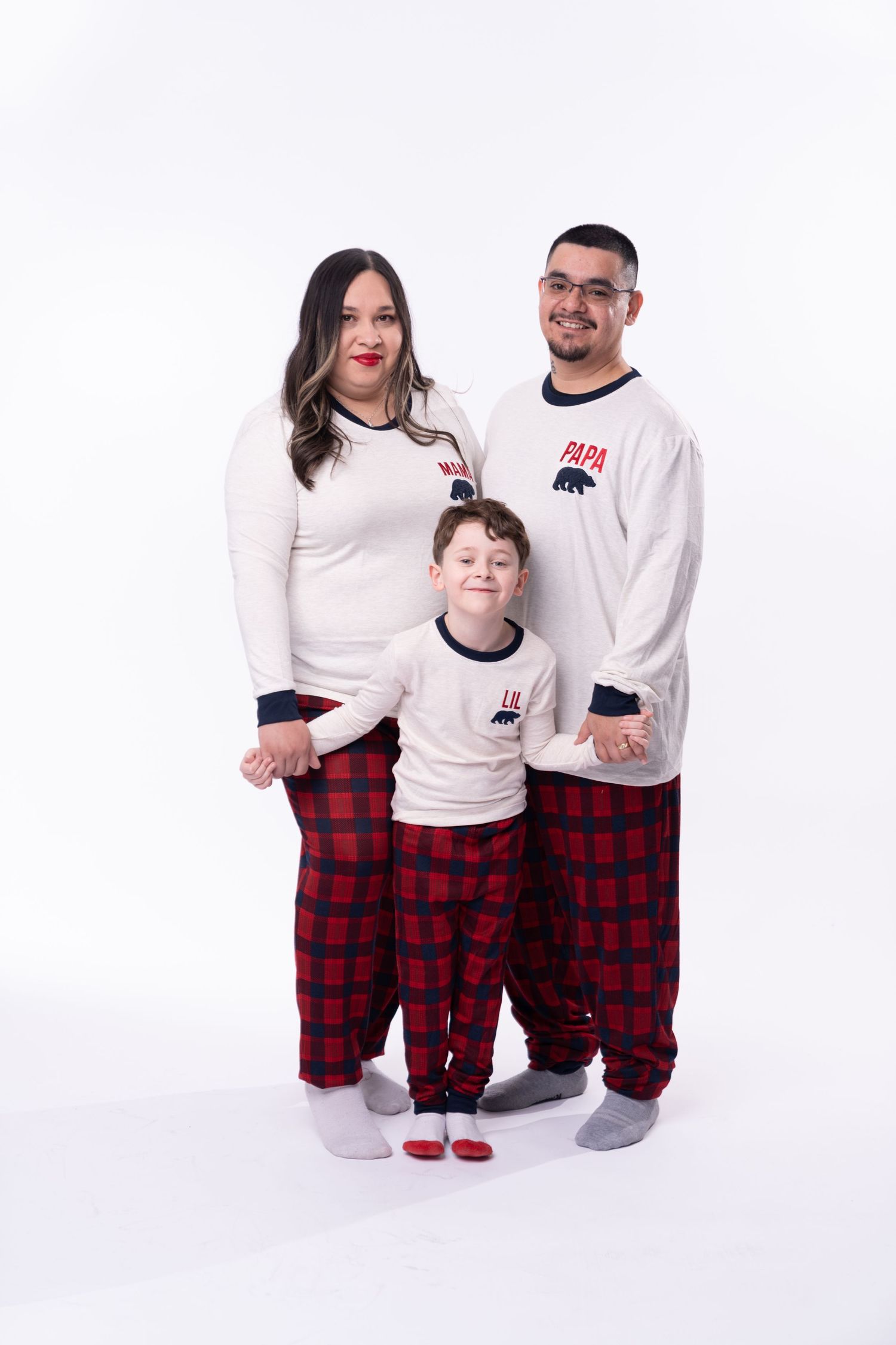 Family wearing coordinated white tops and plaid pajama bottoms pose together.