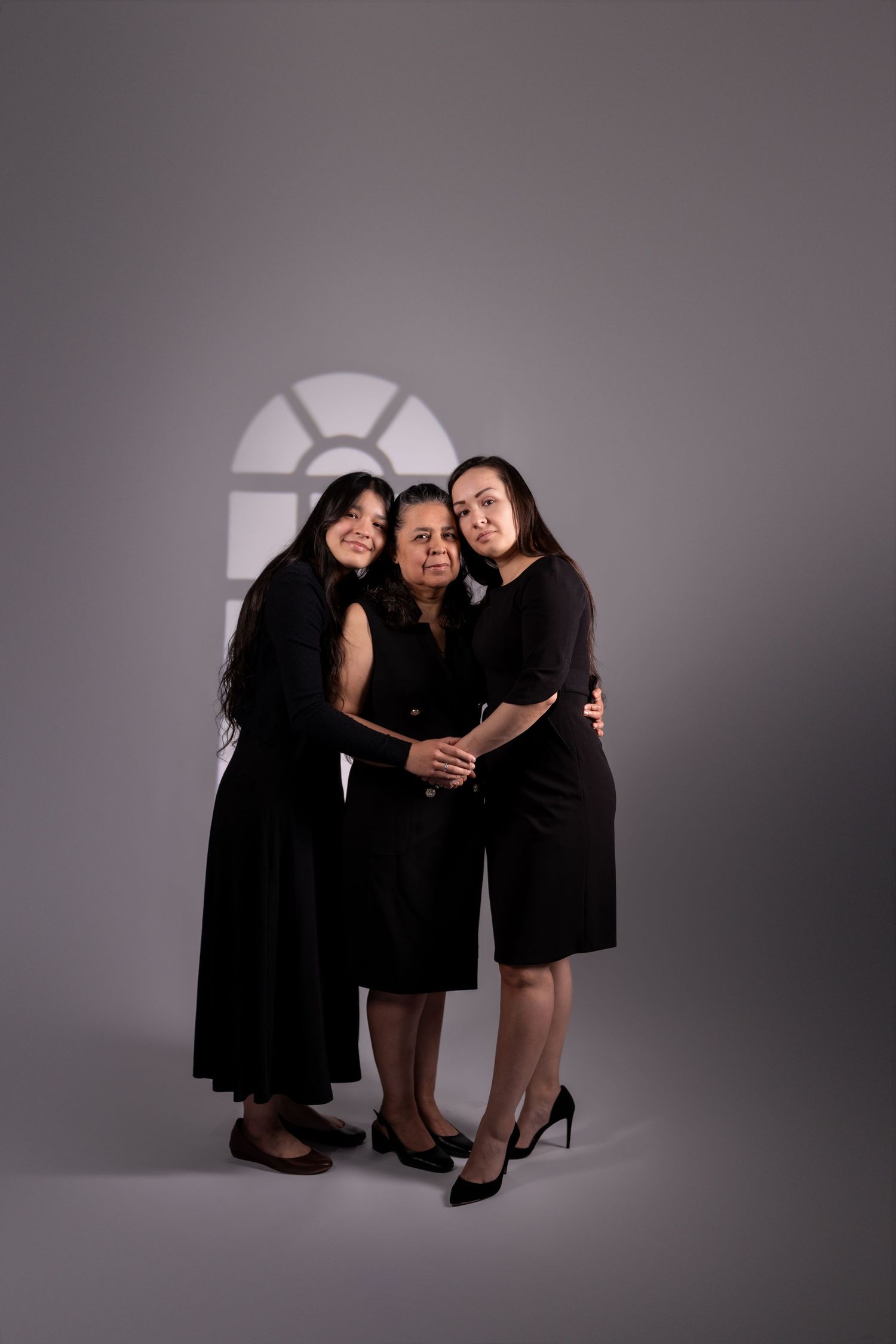 Group portrait in black dresses against grey studio backdrop with window lighting.