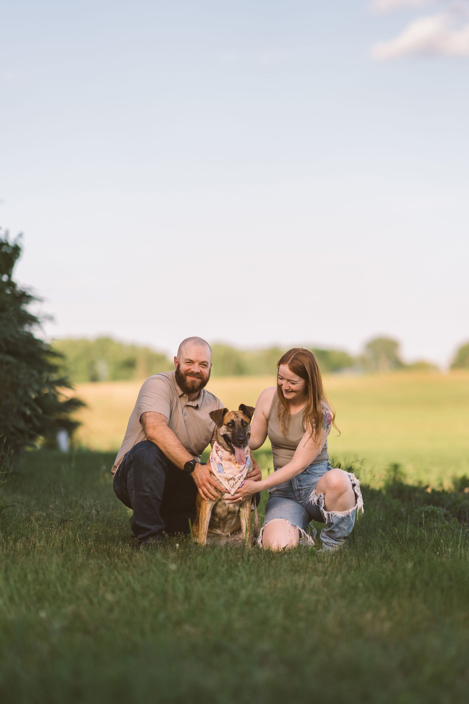 A couple sits with their brown dog on grass during a warm summer evening.