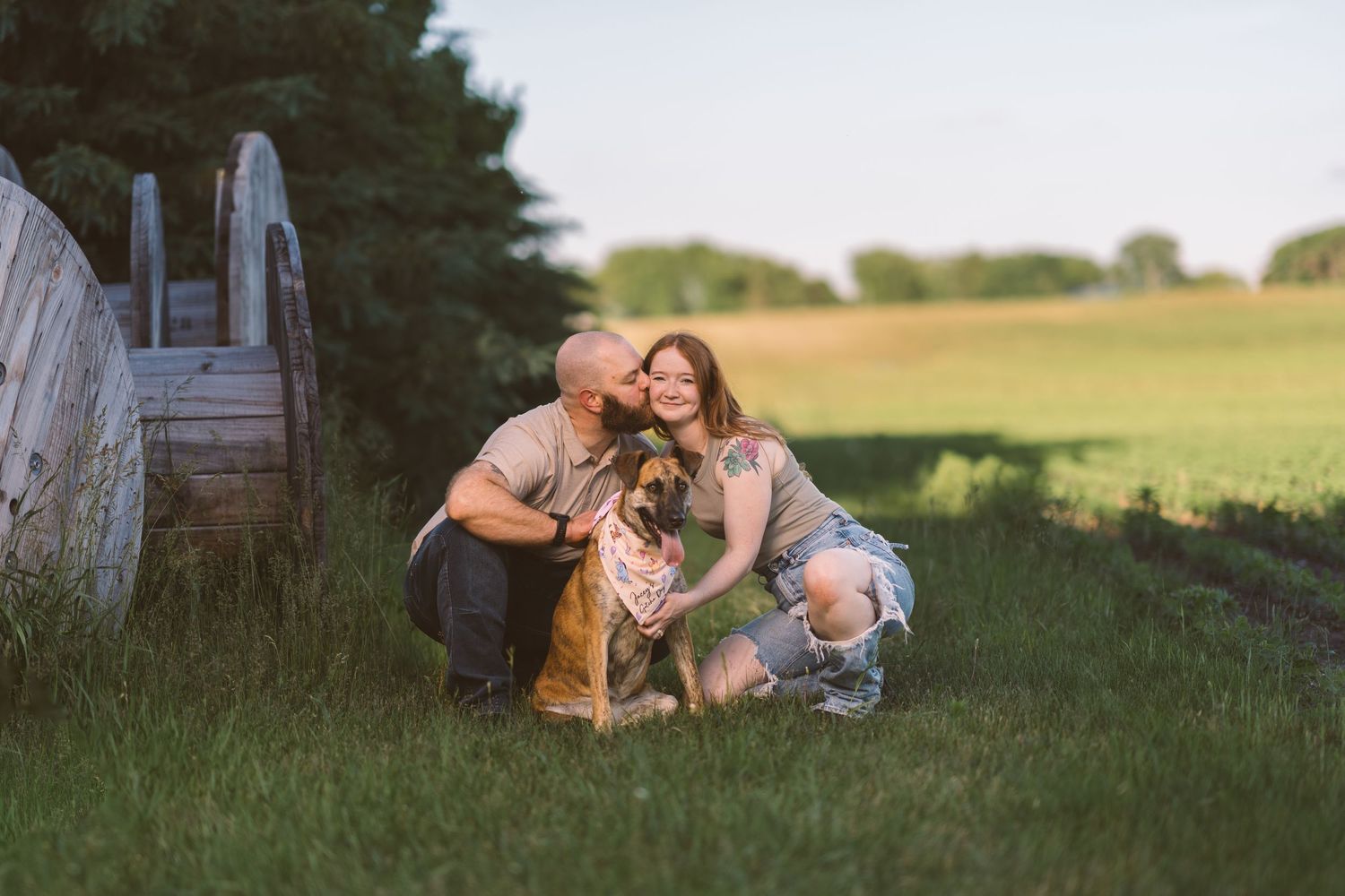 A couple shares a tender moment with their dog in a peaceful countryside setting.