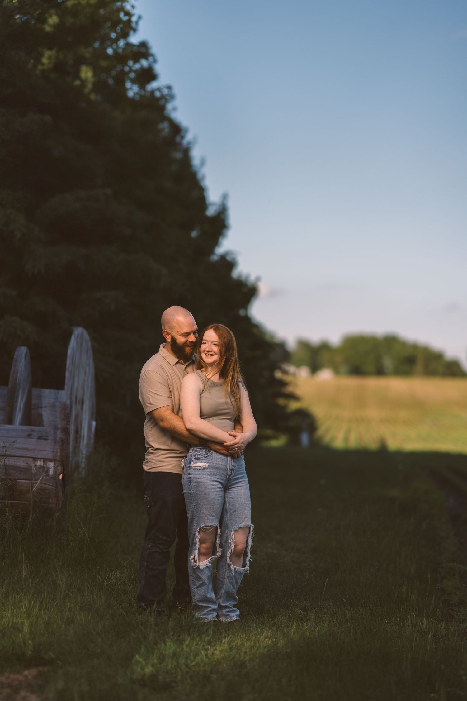 A couple shares an intimate moment in a field during sunset with trees in the background.