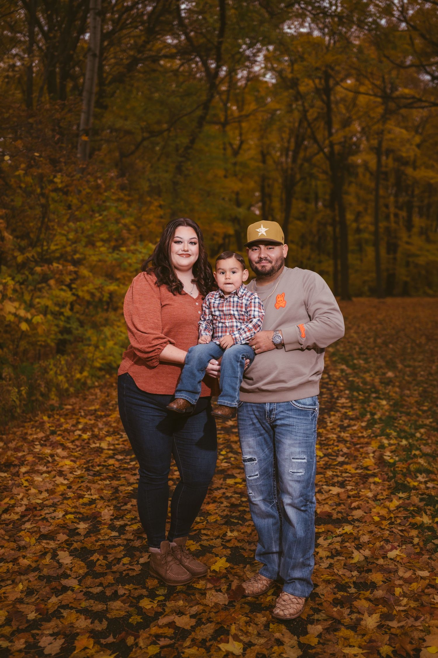A family enjoys an autumn day together among fallen leaves in the woods.