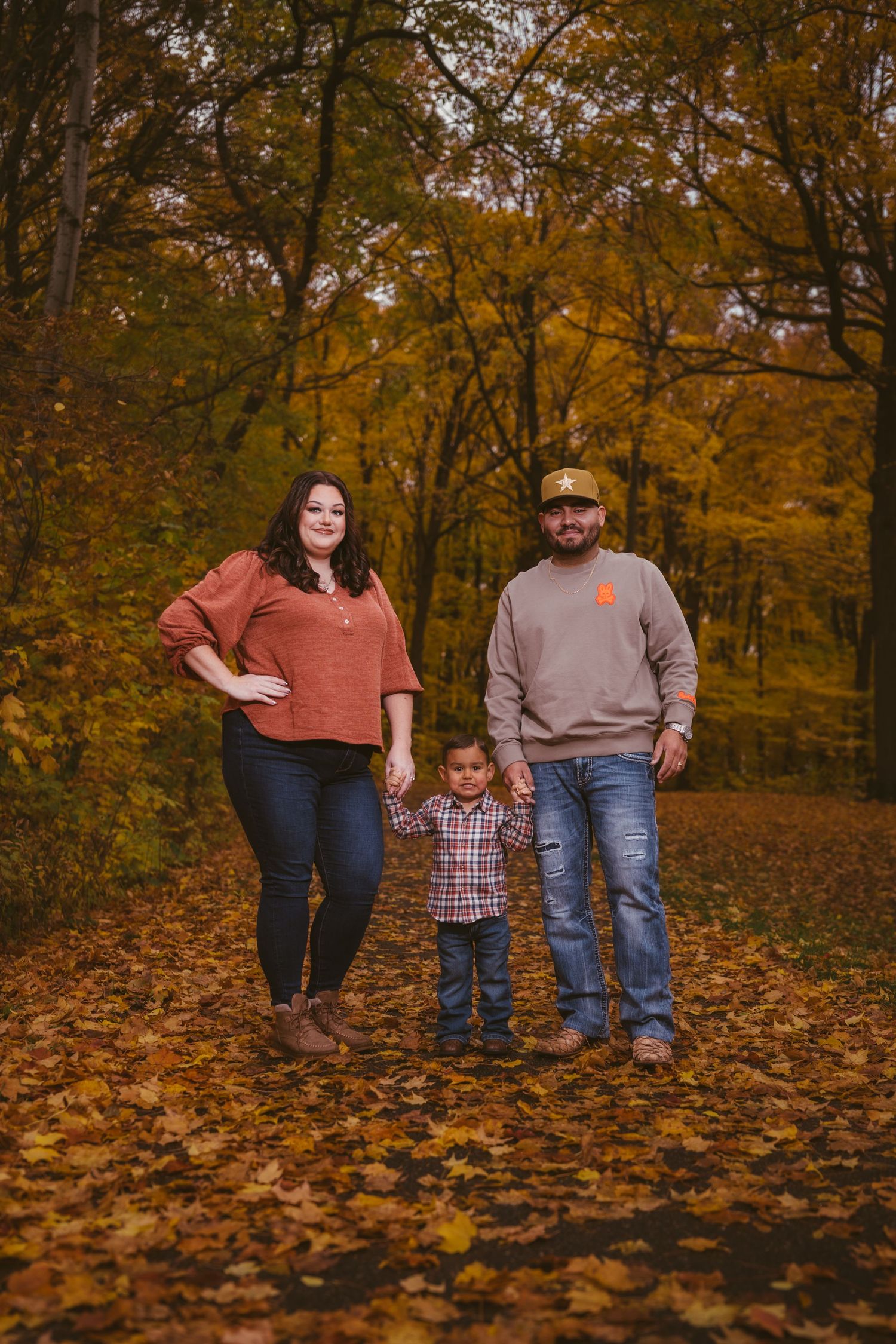 Three people stand together on fallen autumn leaves in a wooded setting.
