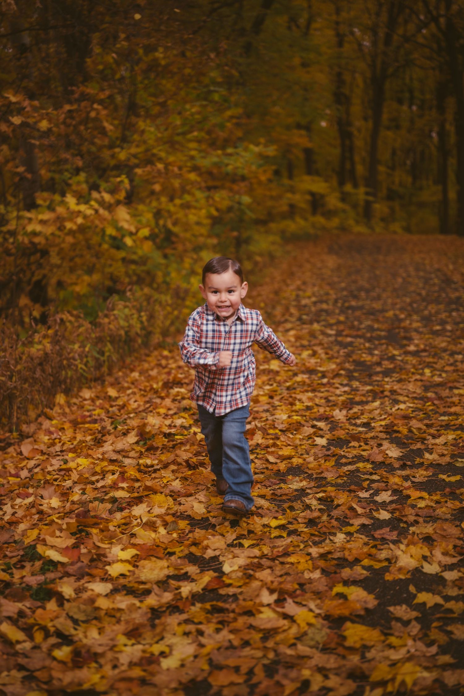 A child runs playfully through fallen autumn leaves in the woods.