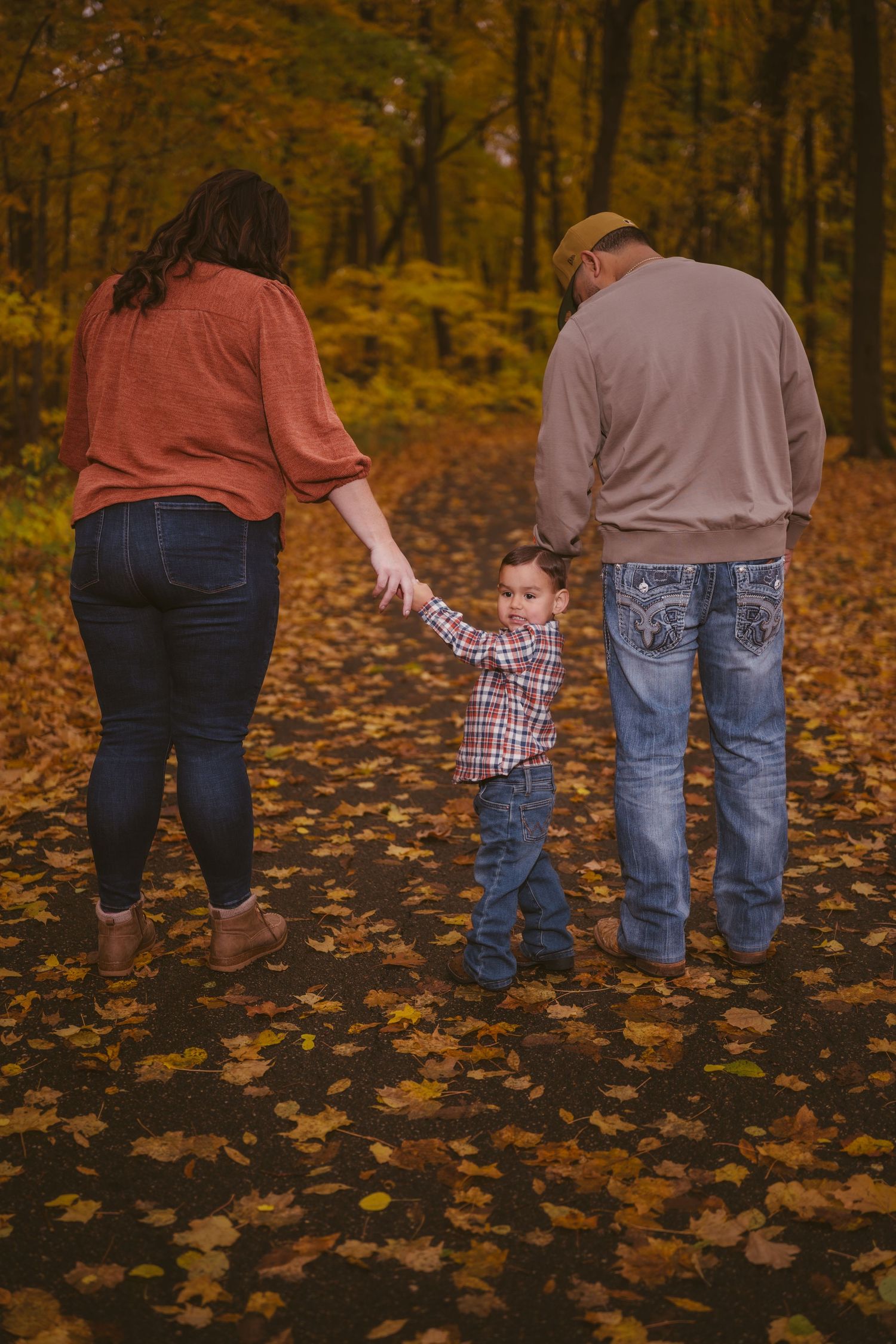People walking together through fallen autumn leaves, photographed from behind.