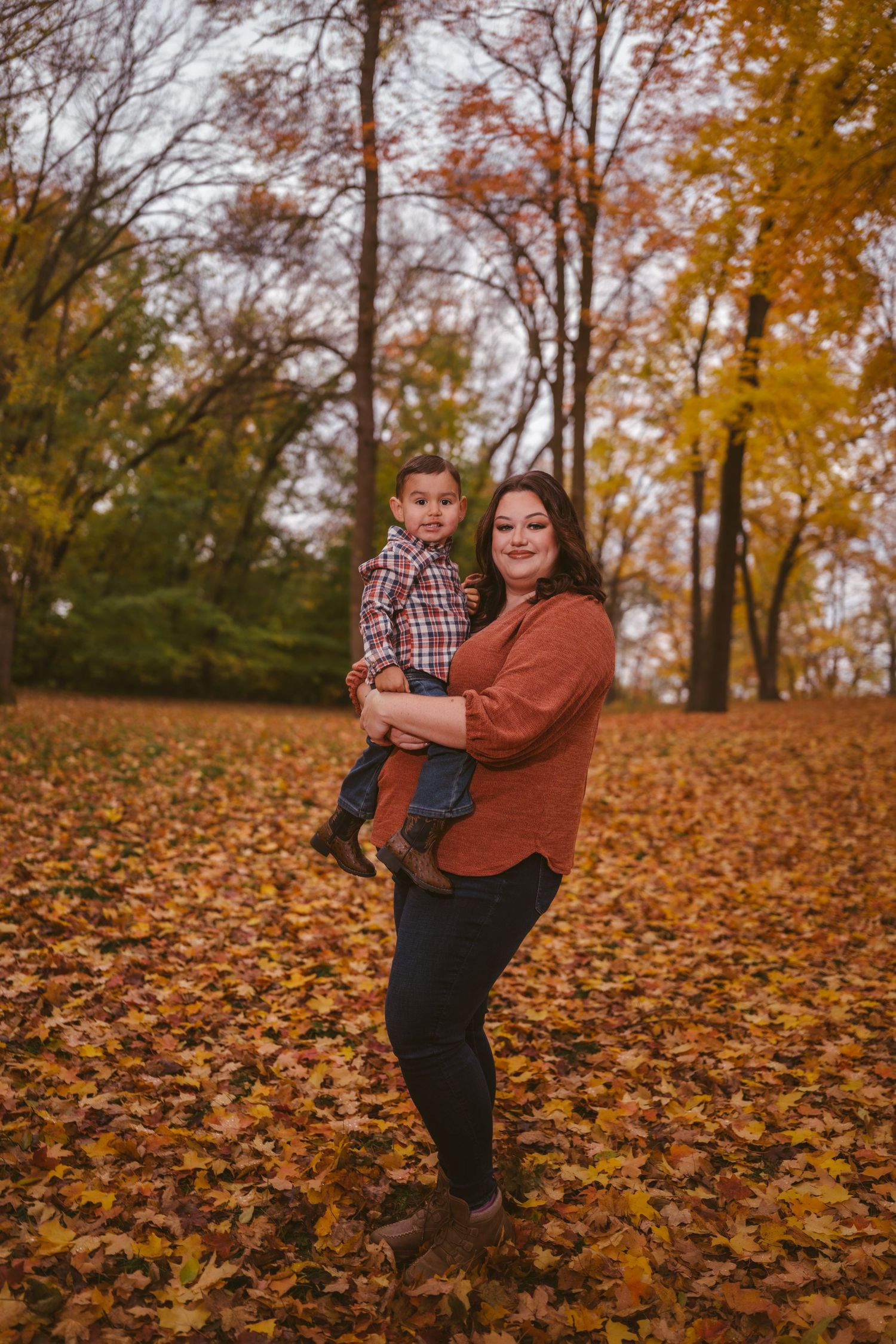 Family portrait session among fallen autumn leaves with warm rust-colored sweater.