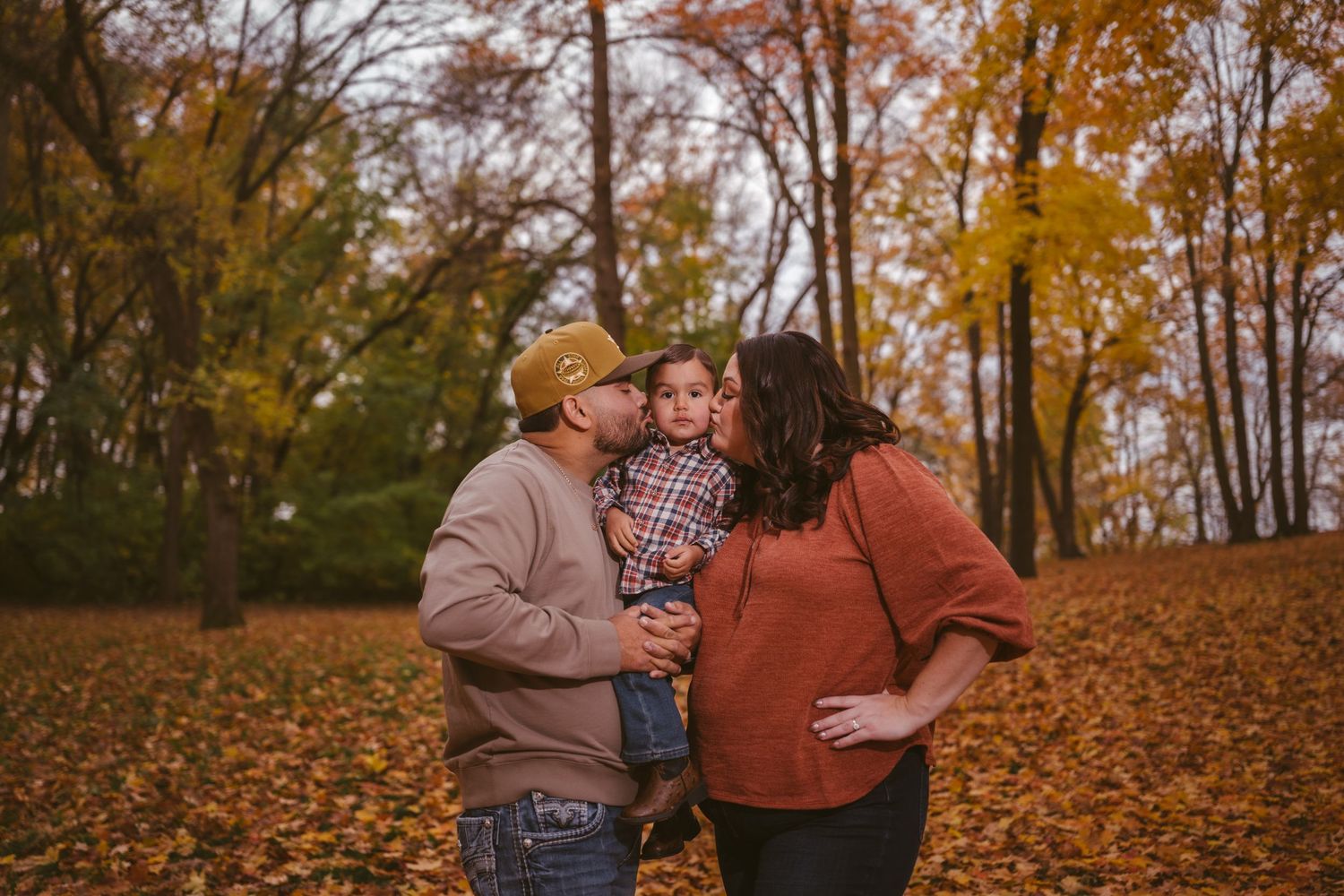 Autumn family photography session with casual poses on leaf-covered ground.