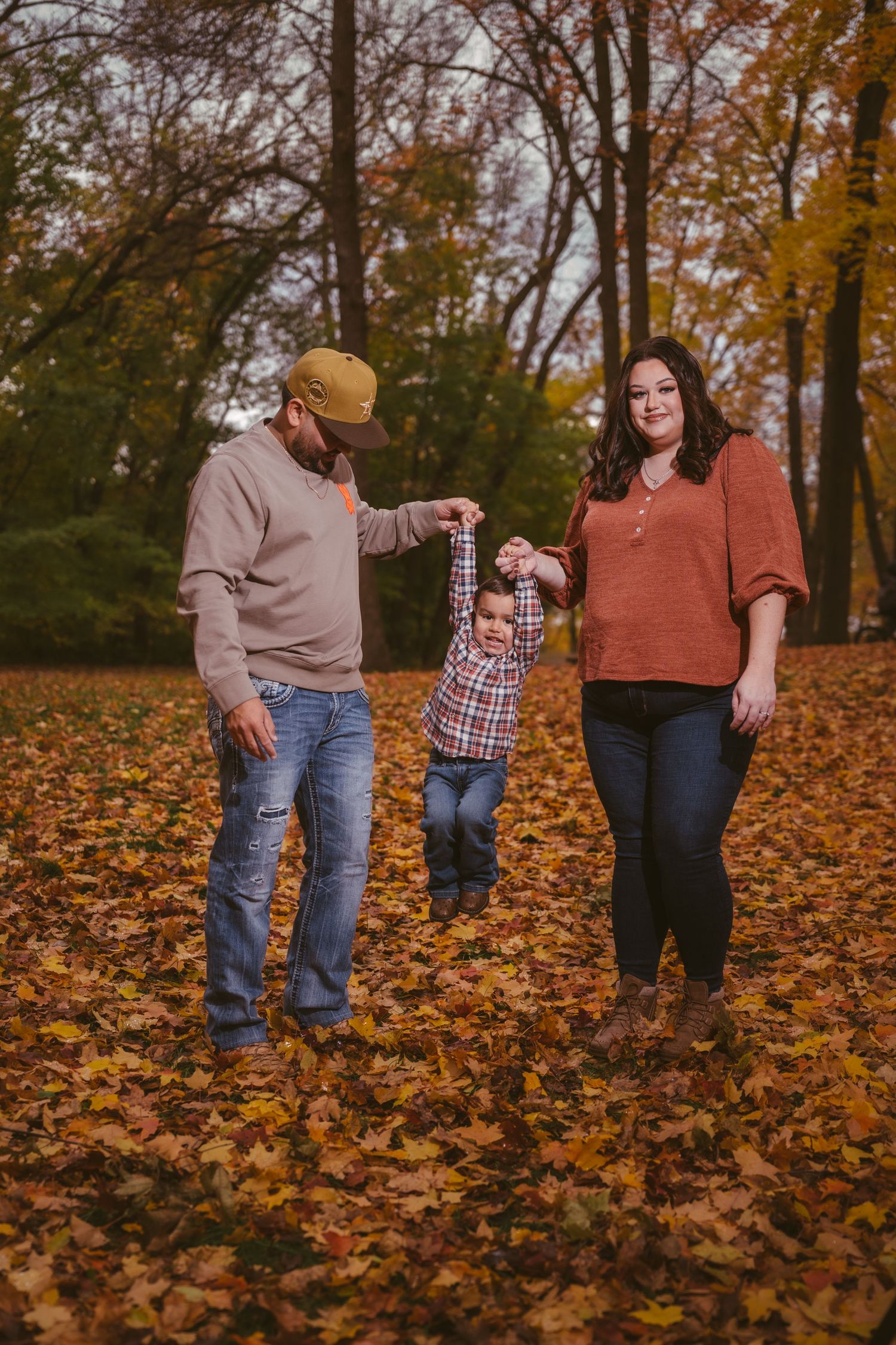 Family members walking through fallen autumn leaves in a forest setting.